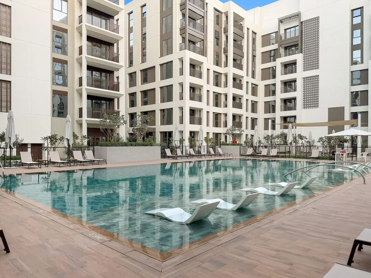 An outdoor swimming pool sits beside a modern multi-story building.