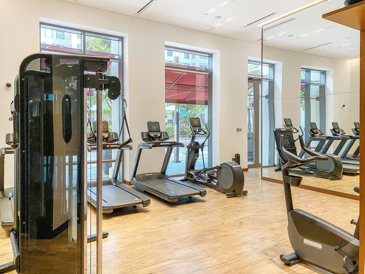 A gym with cardio machines and strength-training equipment beside large windows.