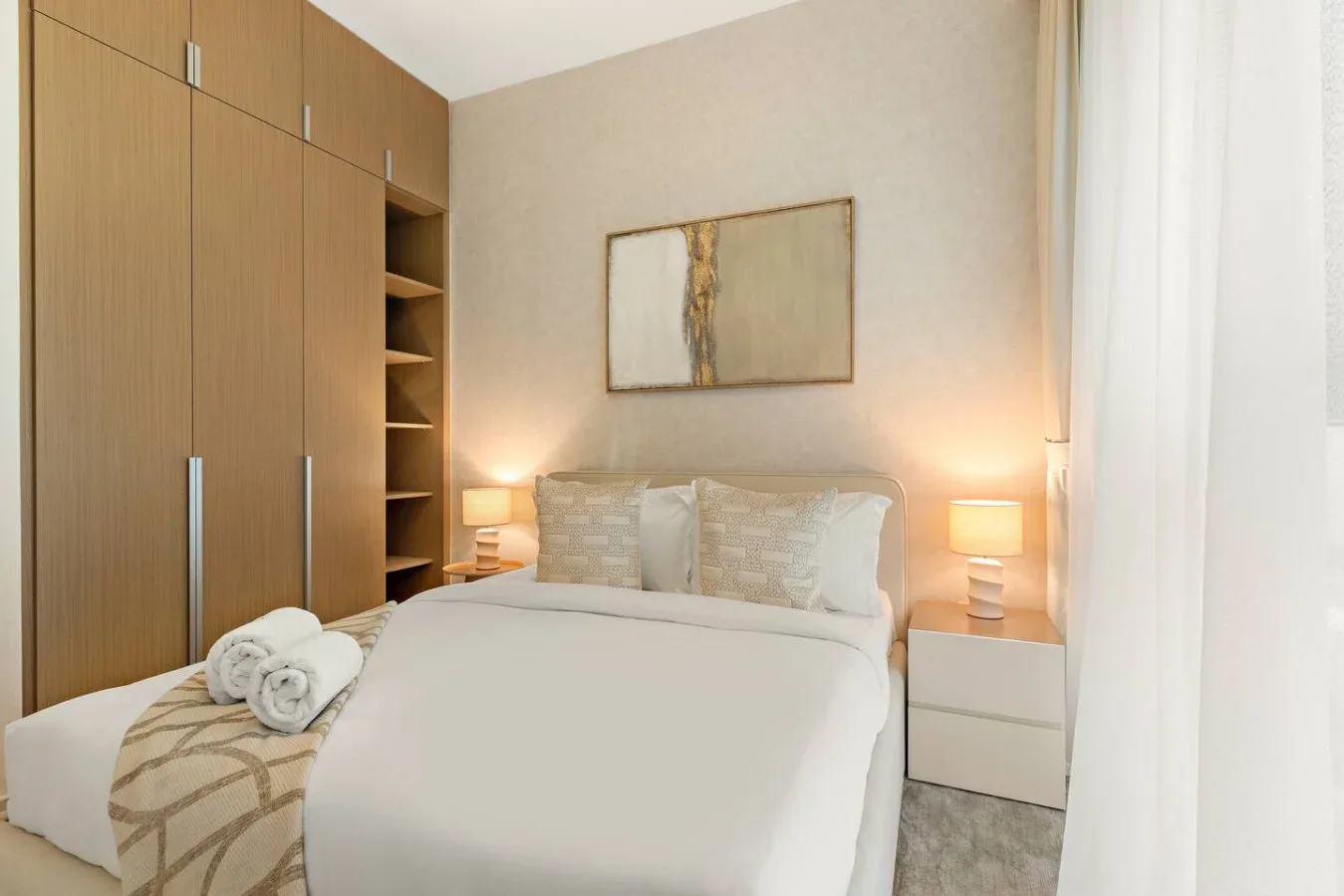A bedroom with a neatly made bed, bedside lamps, and built-in wooden cabinets.