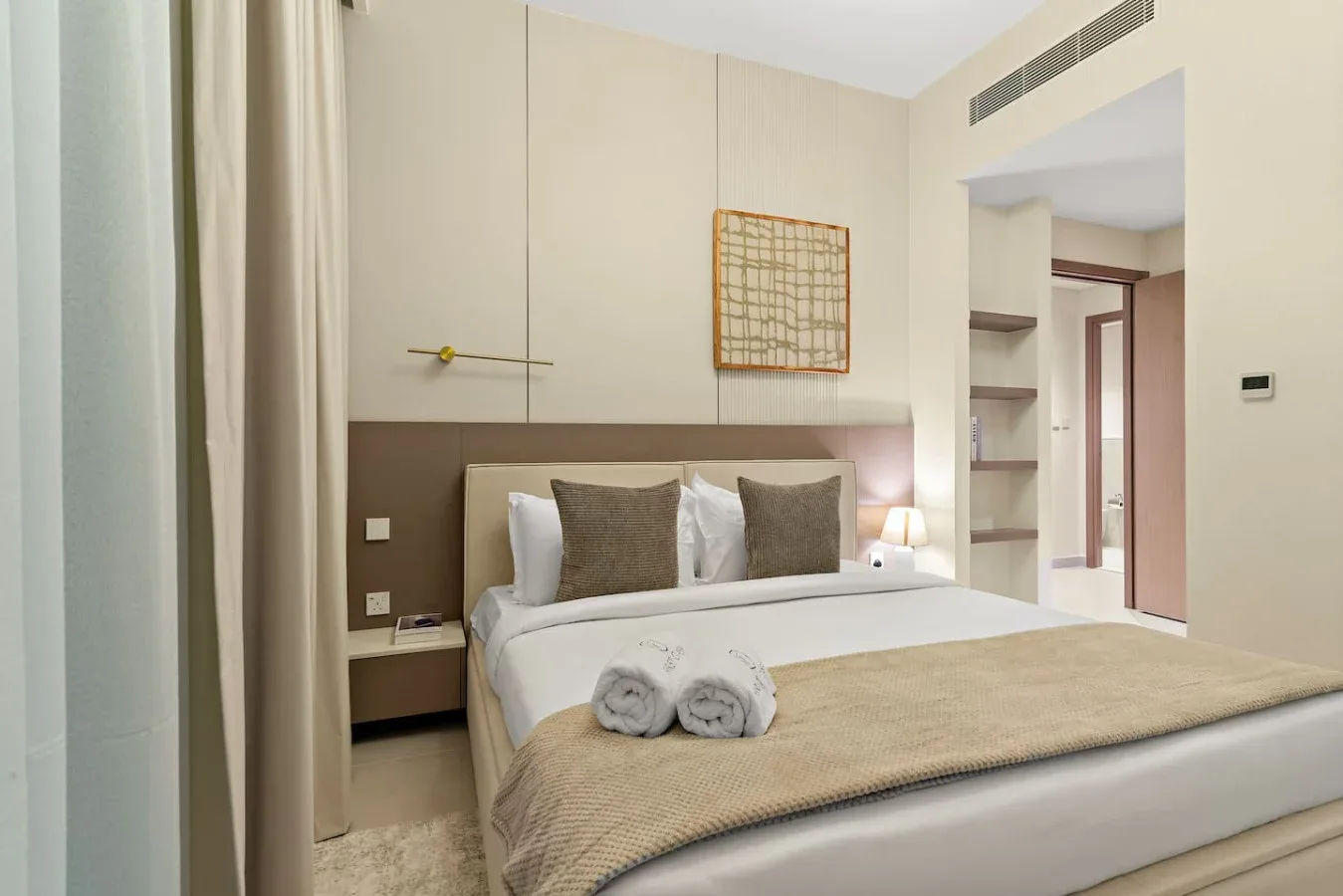 A bright bedroom with a neatly made bed and bedside lighting.