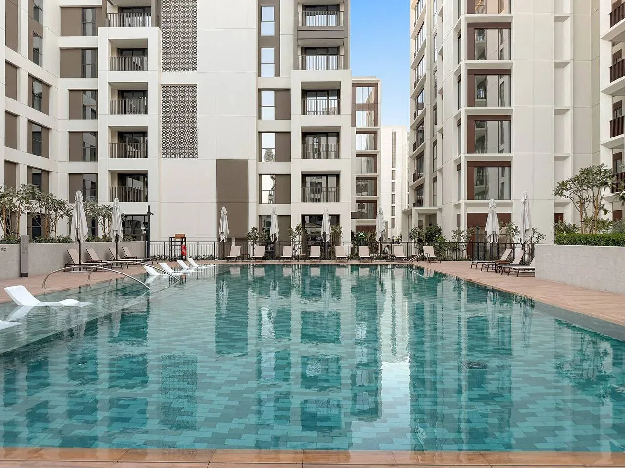 An outdoor swimming pool sits between modern apartment buildings.