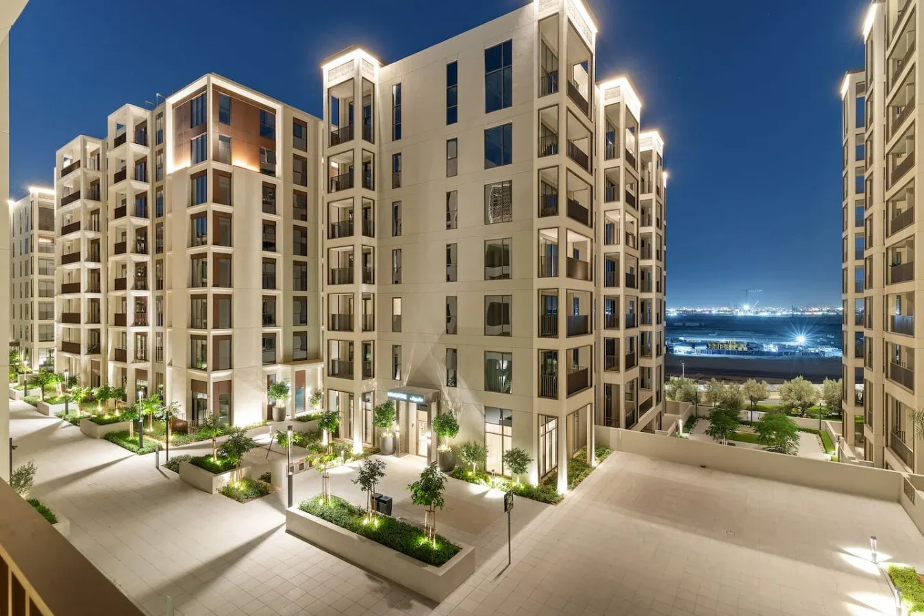 Modern apartment buildings surround a landscaped courtyard at night.