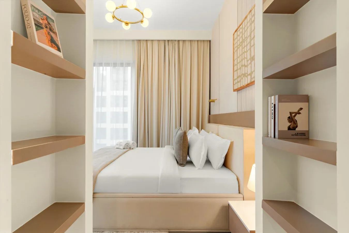 A bedroom with a neatly made bed, beige curtains, and built-in shelving.