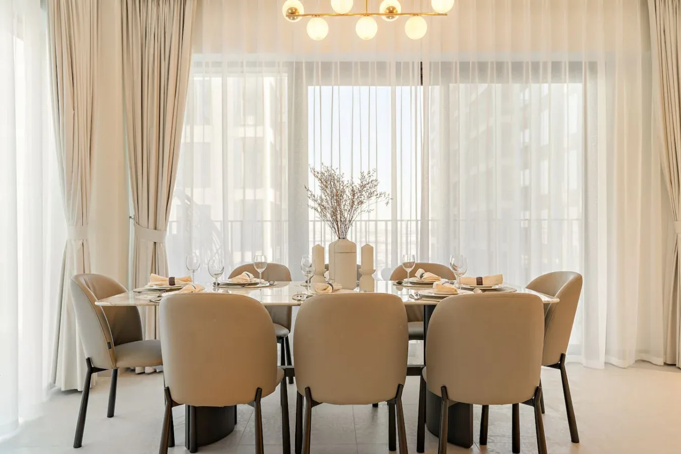 A dining area with a set table and upholstered seating beside tall windows.