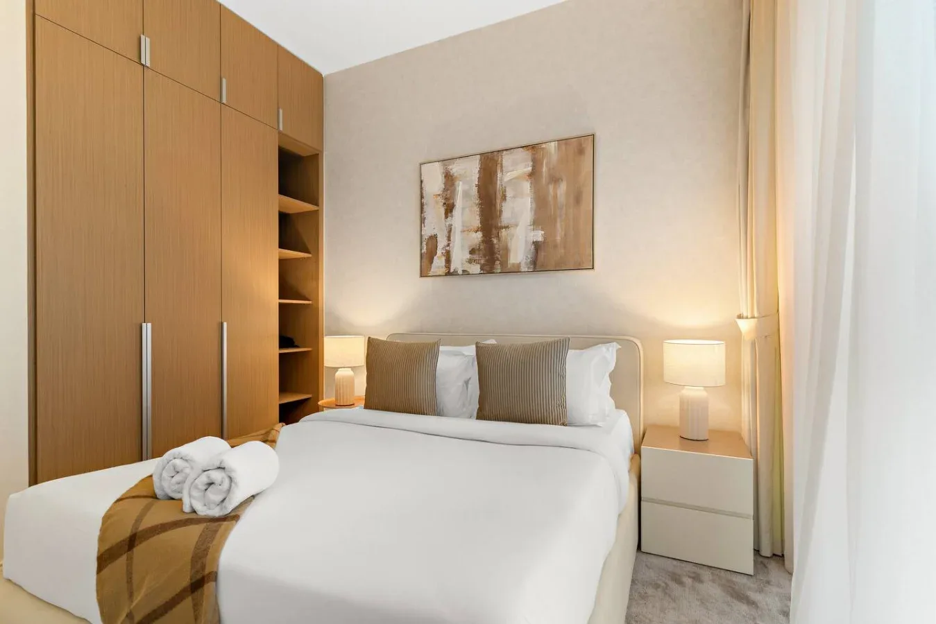 A bedroom with a neatly made bed, bedside tables, and abstract wall art.