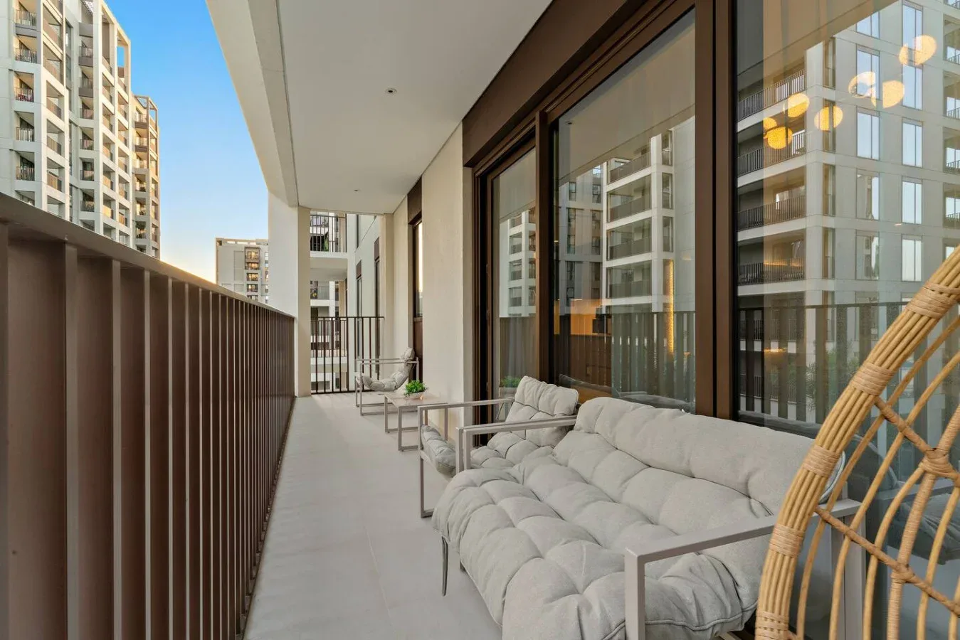 A balcony seating area beside large glass windows, with a cushioned sofa and hanging chair.