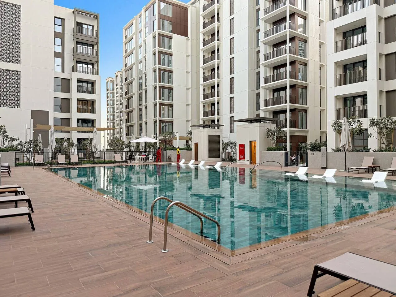 An outdoor swimming pool sits among modern apartment buildings, with loungers along the deck.