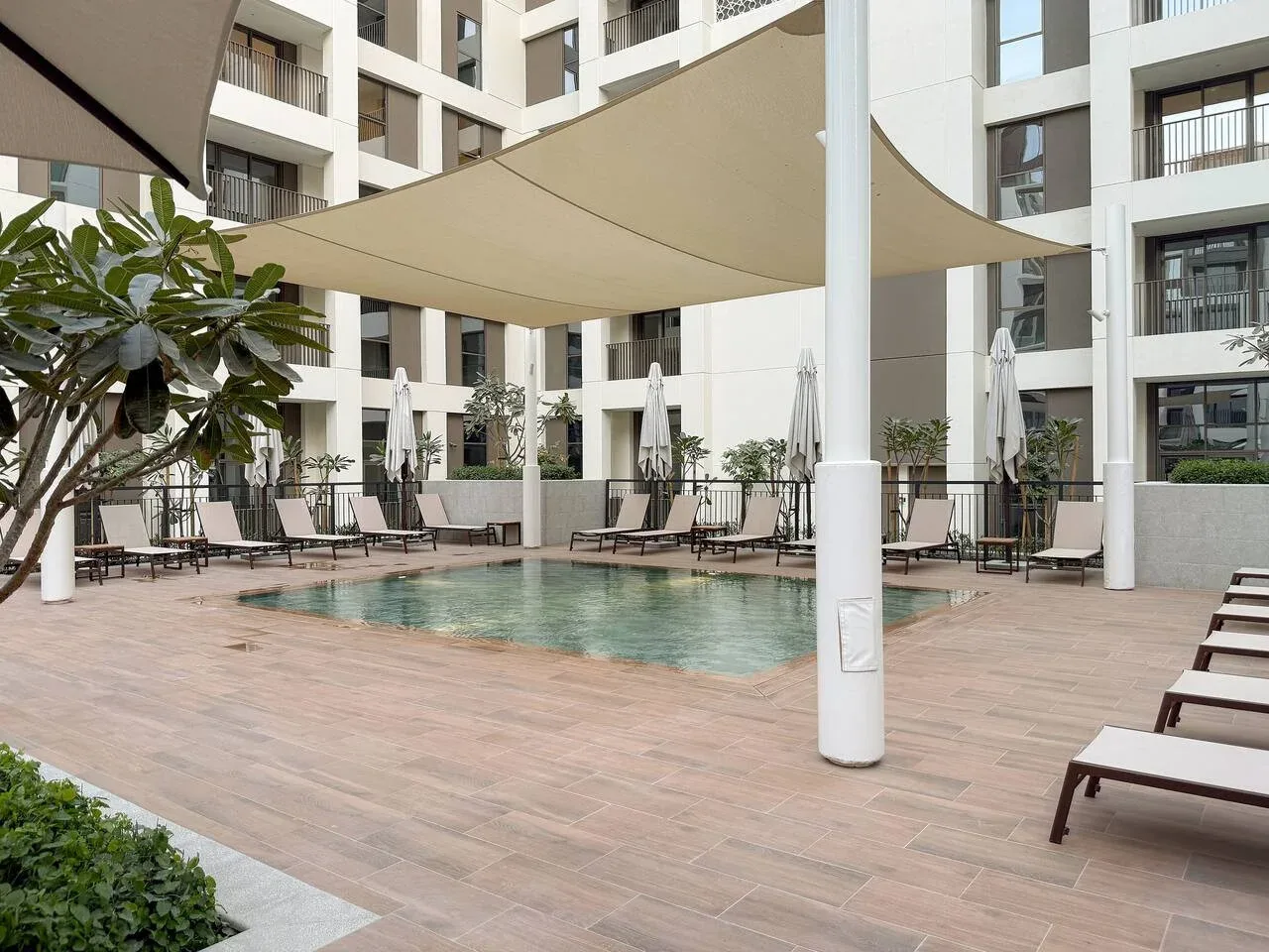An outdoor pool courtyard with shade canopies and surrounding seating.