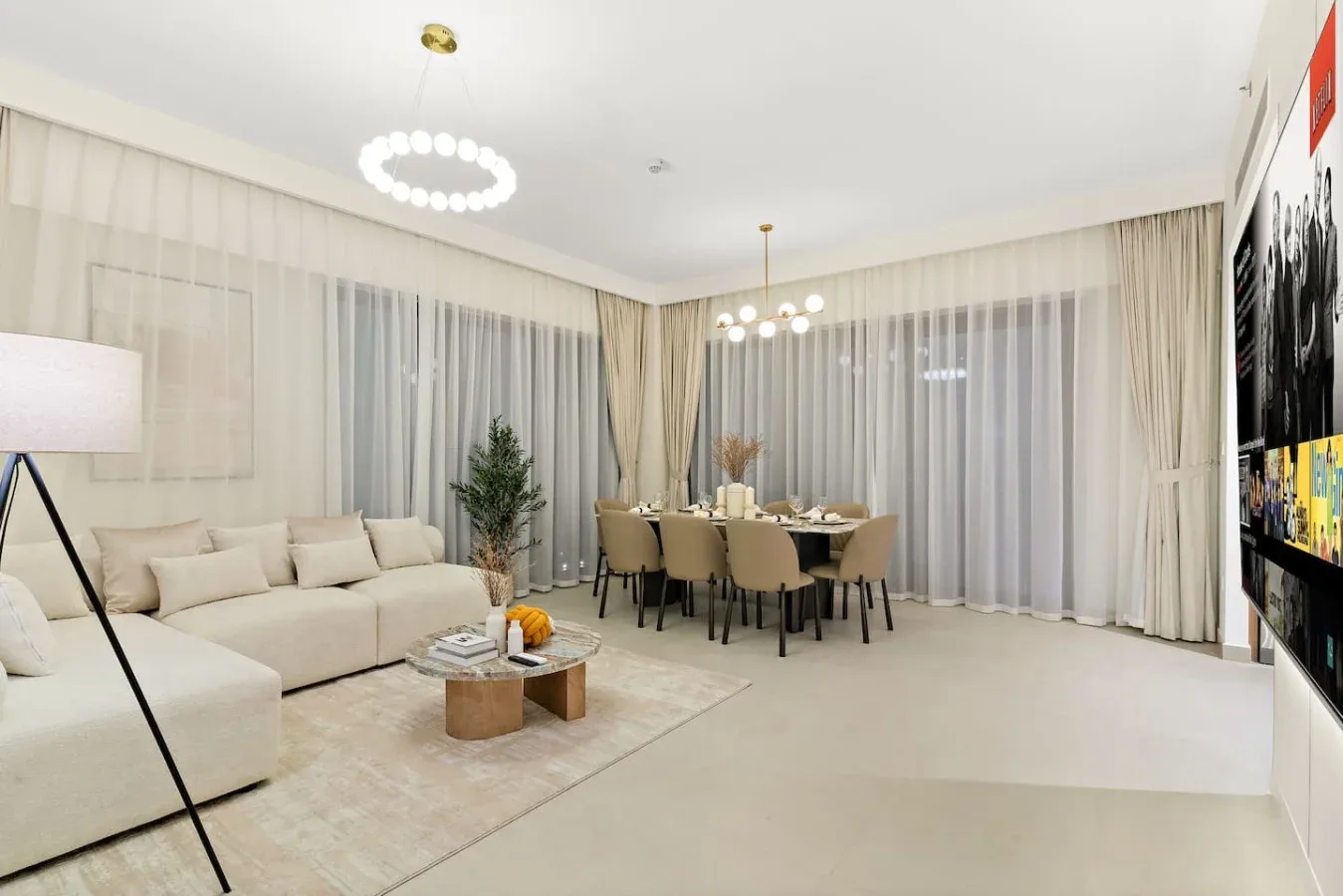 A bright living and dining area with seating, a table, and full-length curtains.