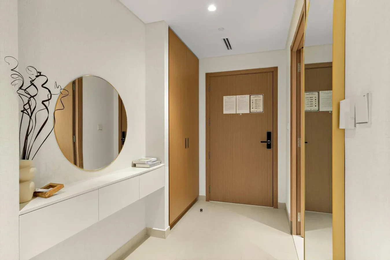 A bright entry hallway with a wood-toned door, round mirror, and built-in console.