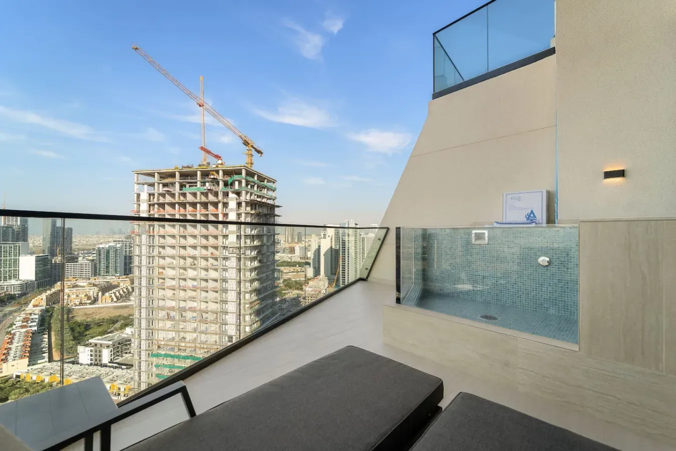 A rooftop terrace with cushioned seating, a glass railing, and a small tiled pool.
