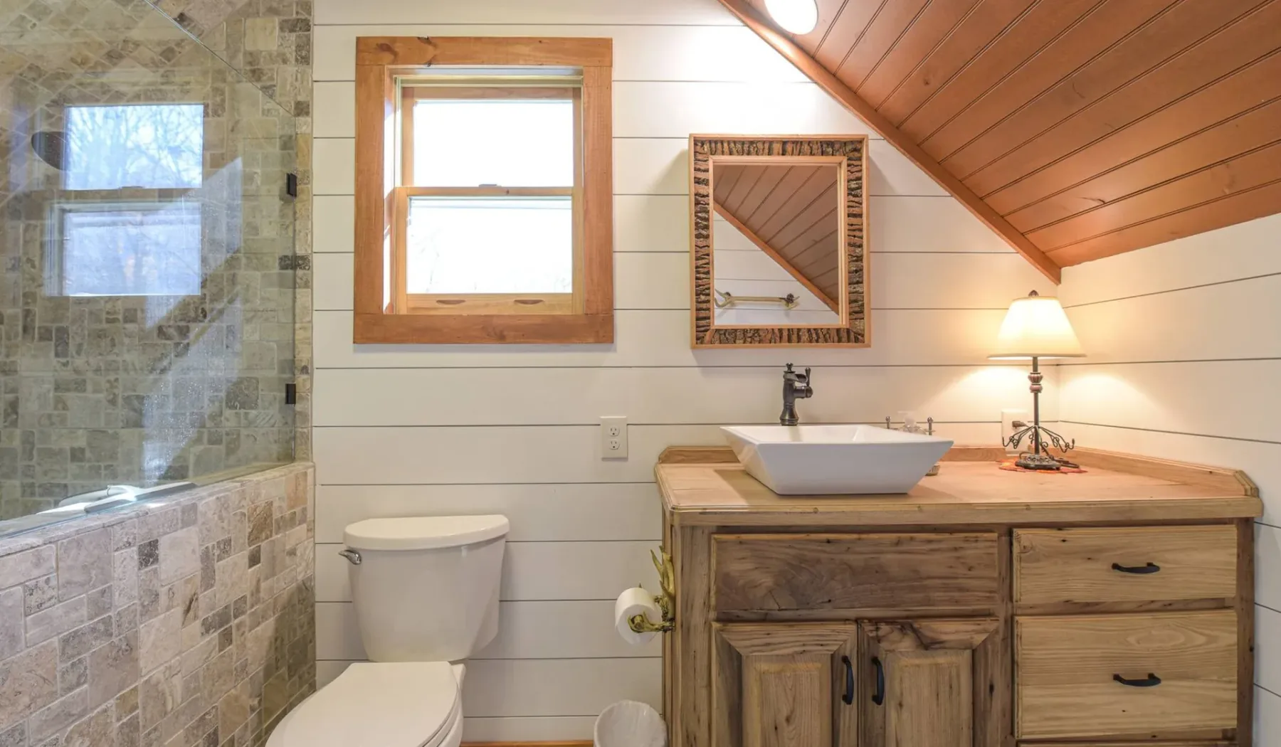 A bathroom with a tiled shower, toilet, and wooden vanity.