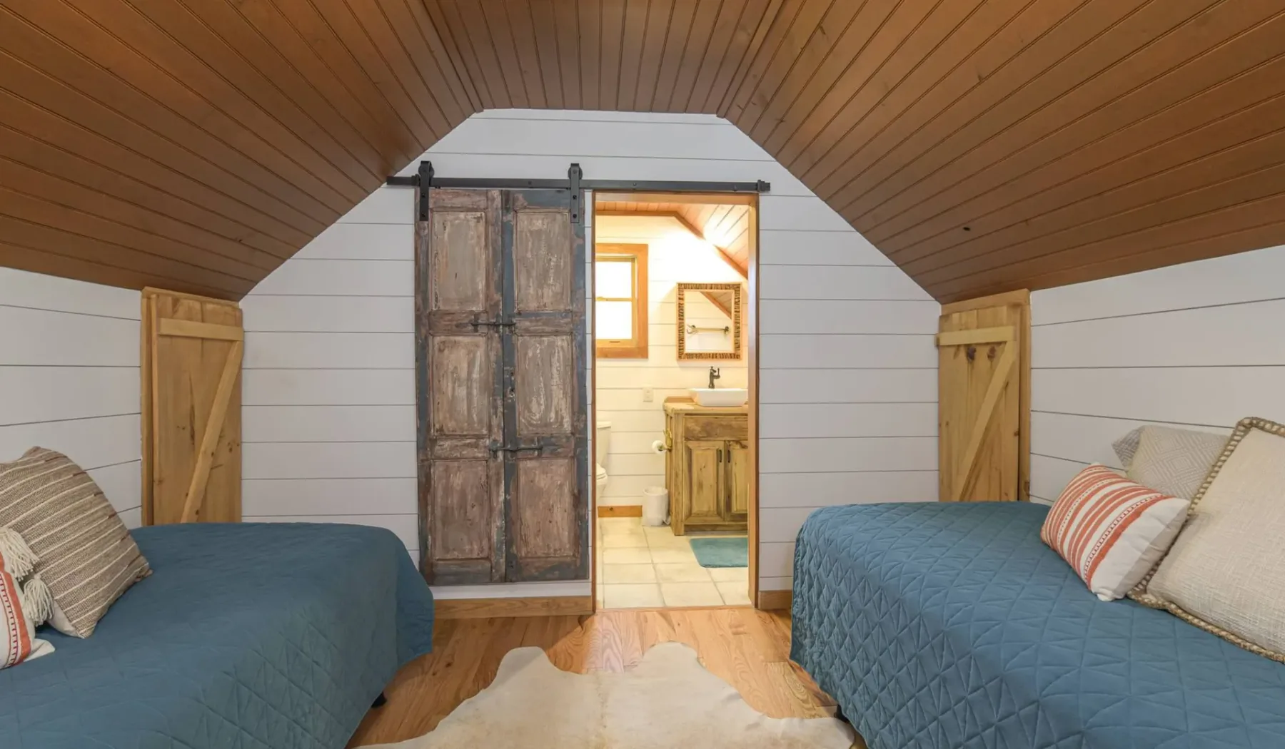 A cozy attic bedroom with two beds and an open doorway to a bright bathroom.