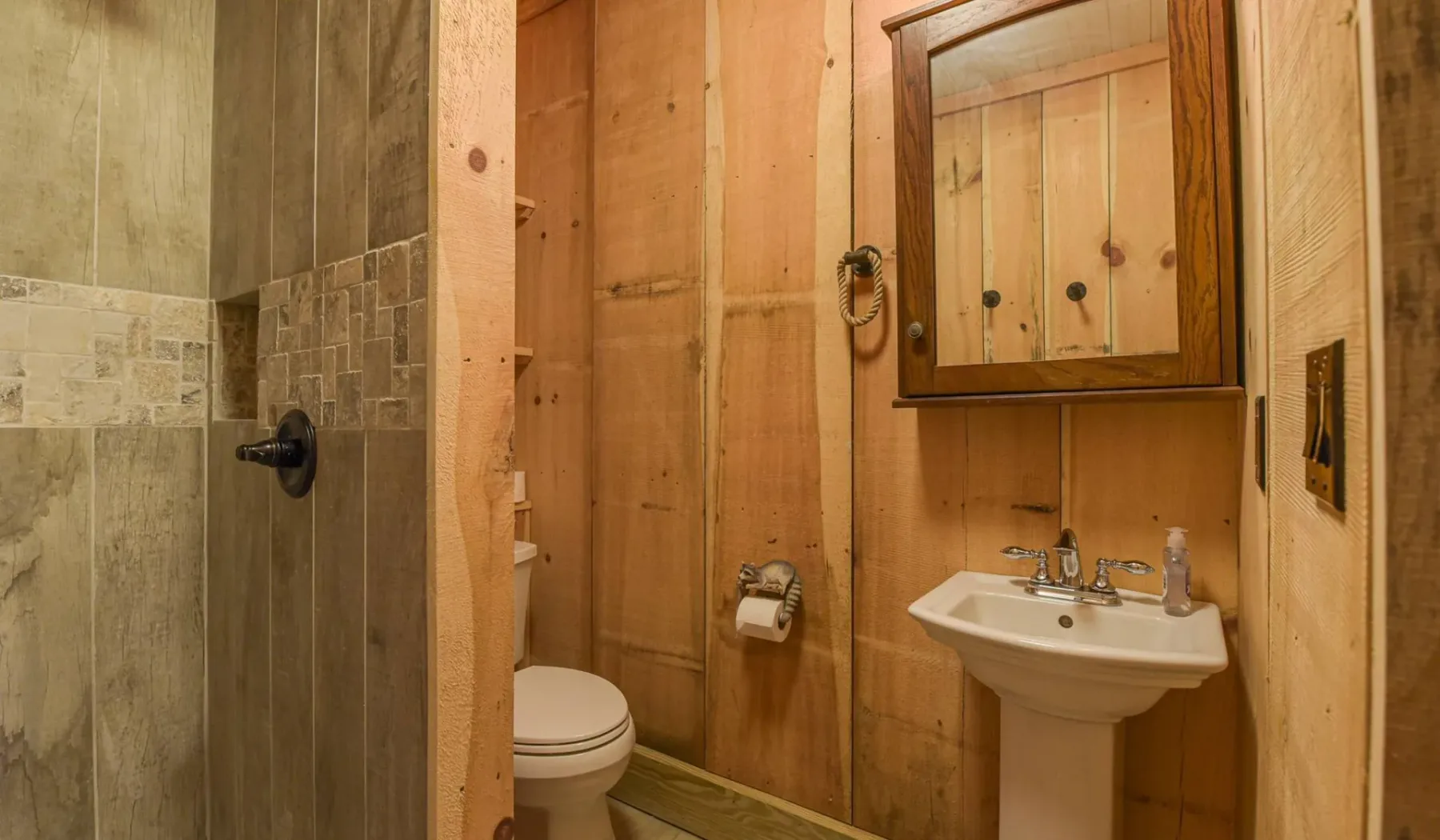 A wood-paneled bathroom with a sink, mirror, and shower.