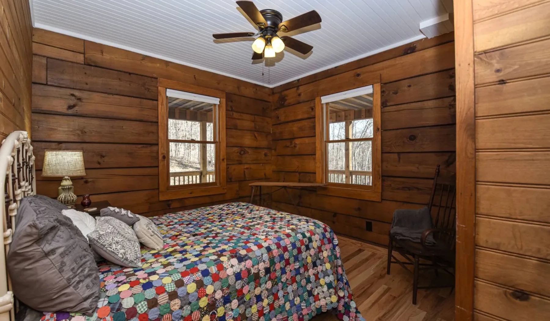 A bedroom with a colorful patchwork bedspread and two windows.