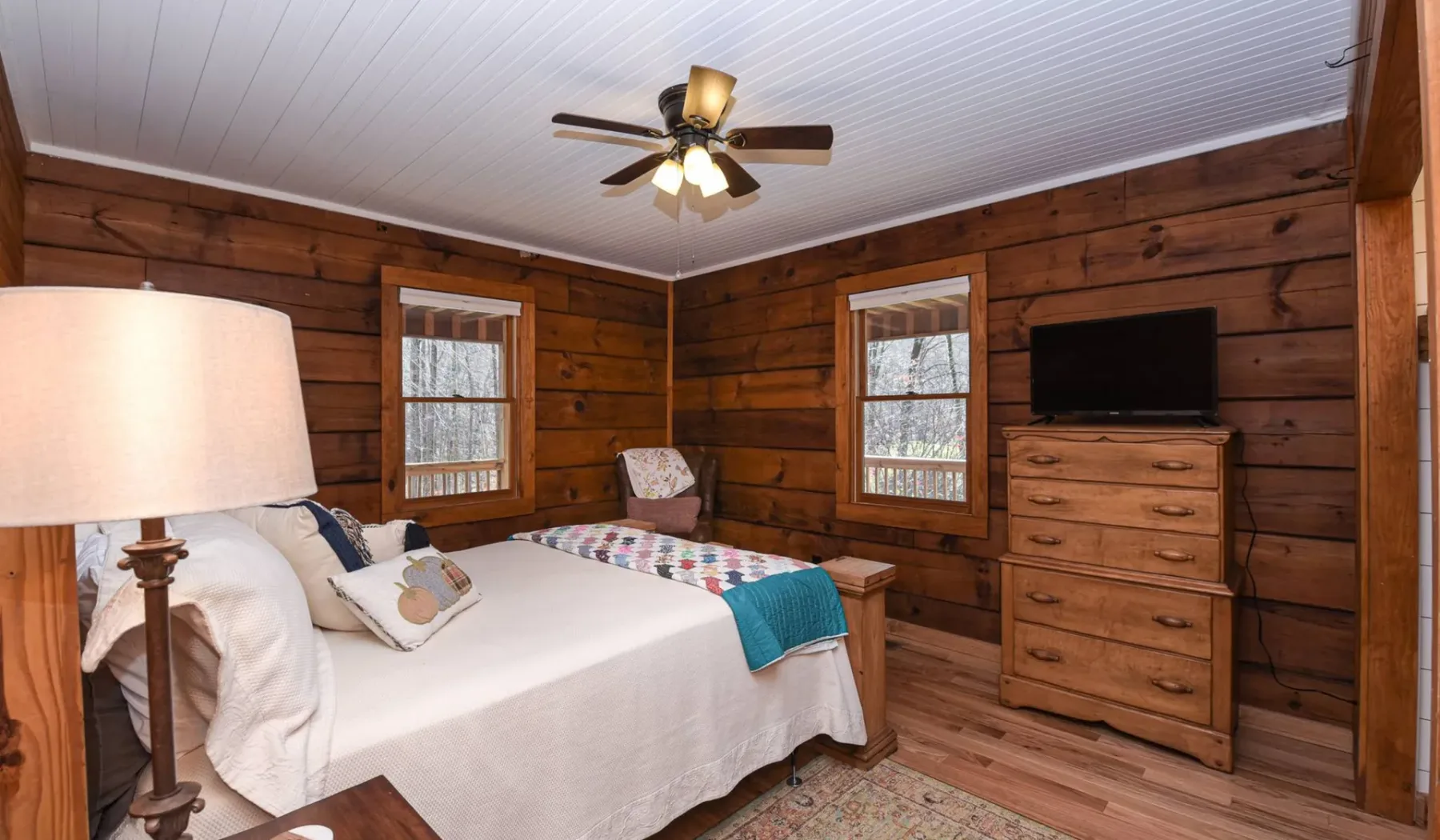 A wood-paneled bedroom with a bed, two windows, and a ceiling fan.