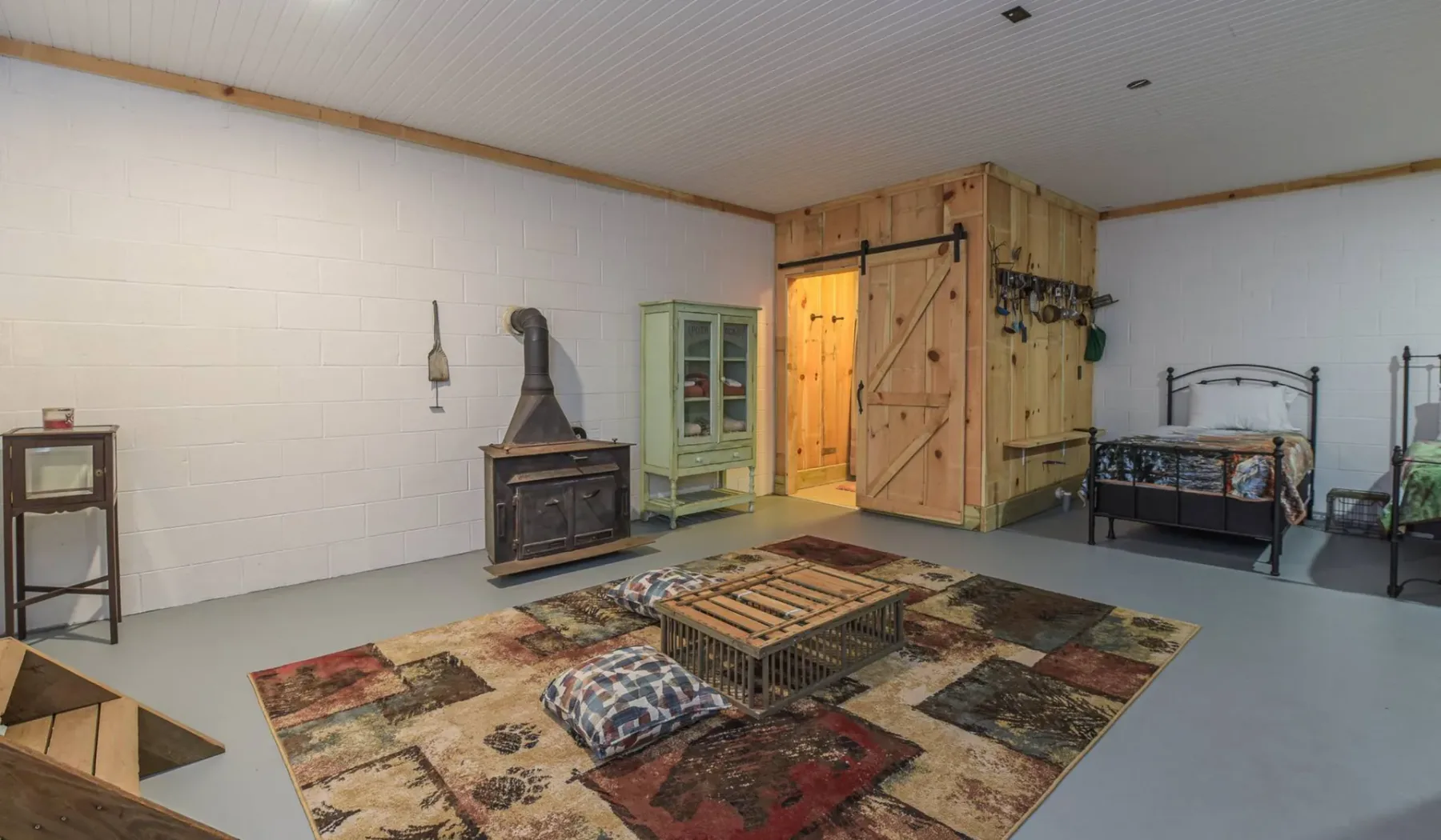 A rustic bedroom with a wood stove, patterned rug, and bed.