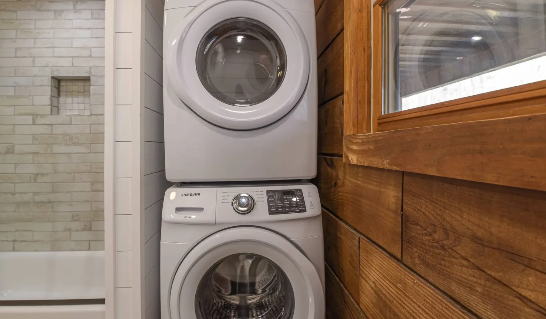 A laundry area with a stacked washer and dryer beside a tiled shower.