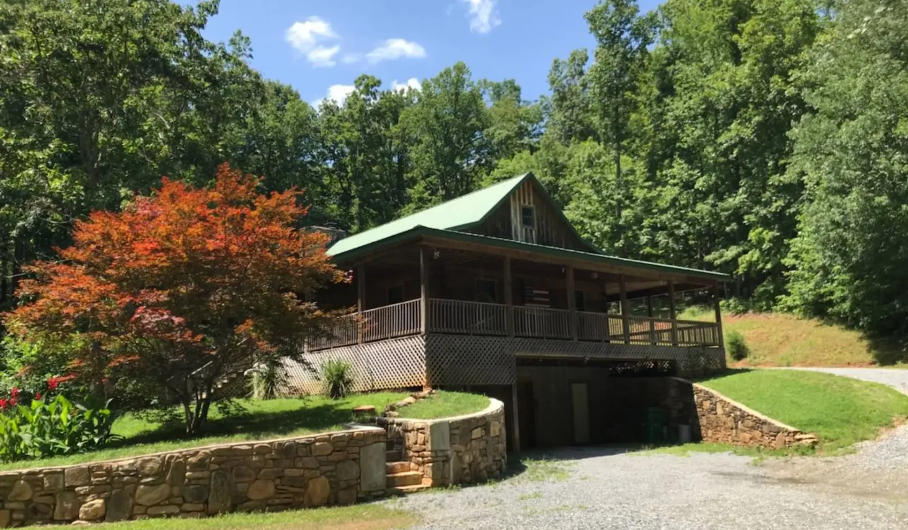 A wooded cabin with a covered porch sits above a stone retaining wall.