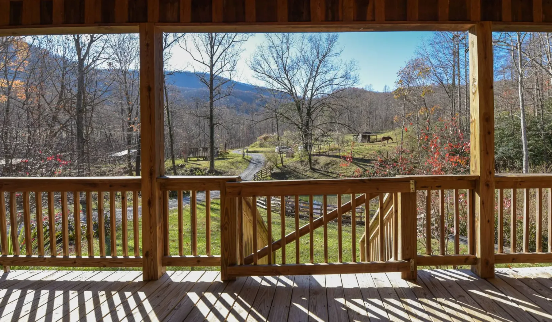 A wooden deck overlooks a grassy yard and wooded hills.