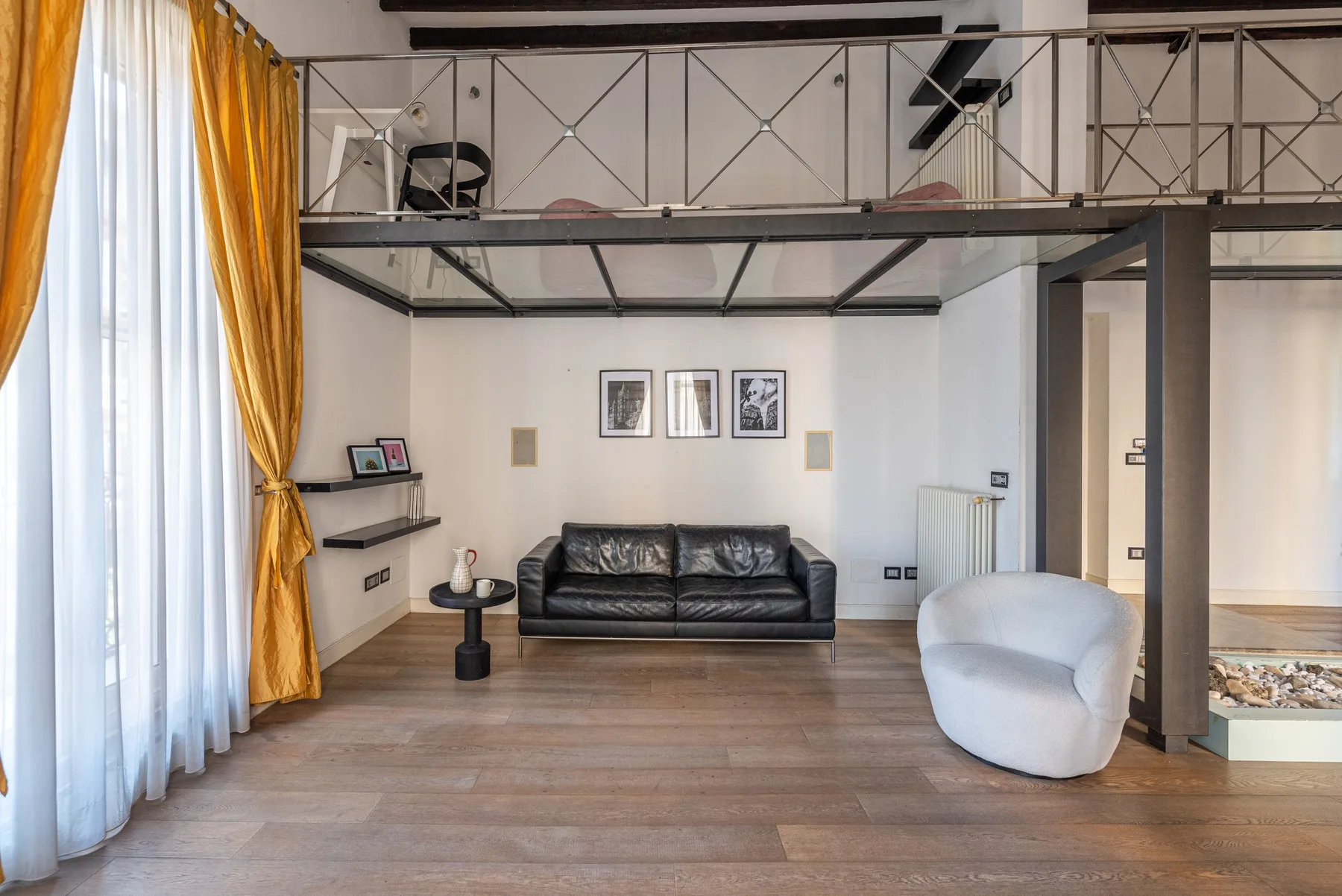 A living room with a black sofa beneath a raised mezzanine.
