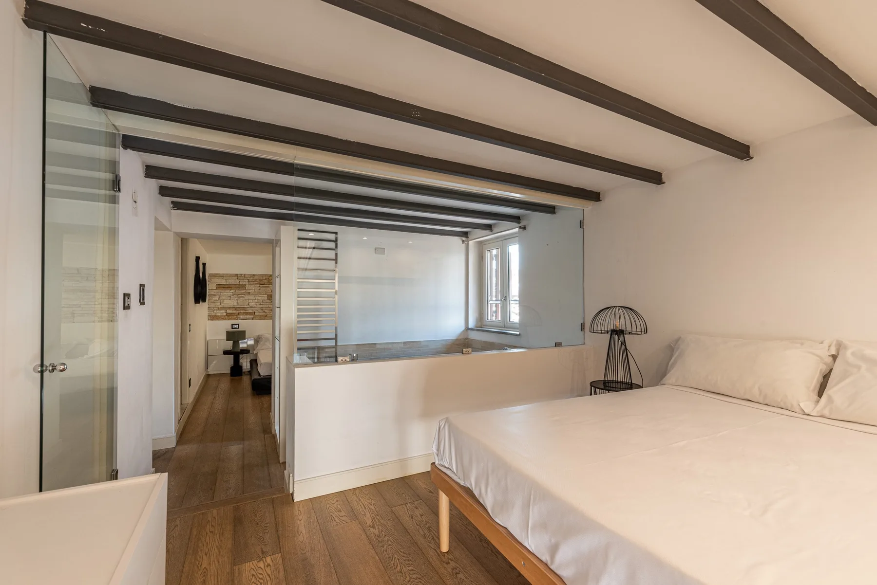 A bedroom with a bed beside a glass partition overlooking a bathroom area.