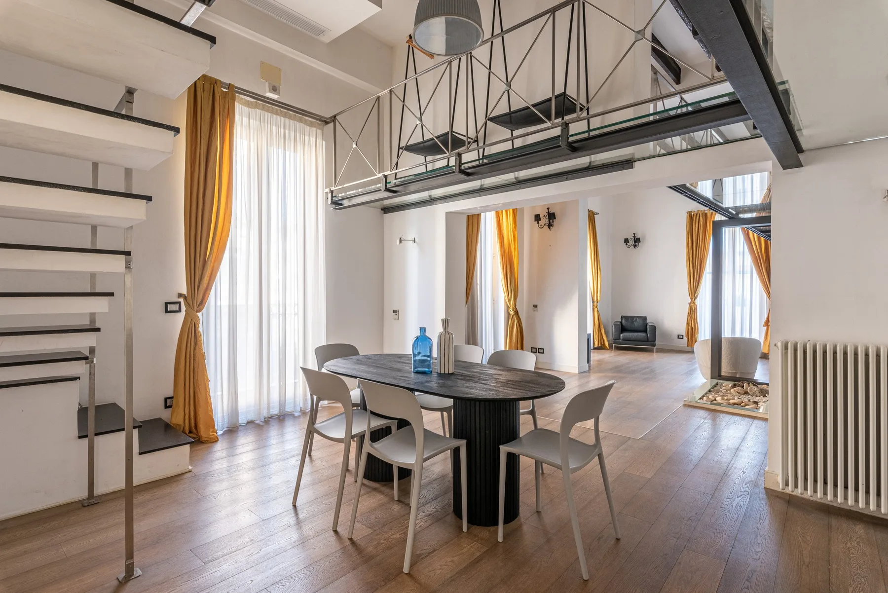 A bright open-plan dining area with a dark table beneath a mezzanine.