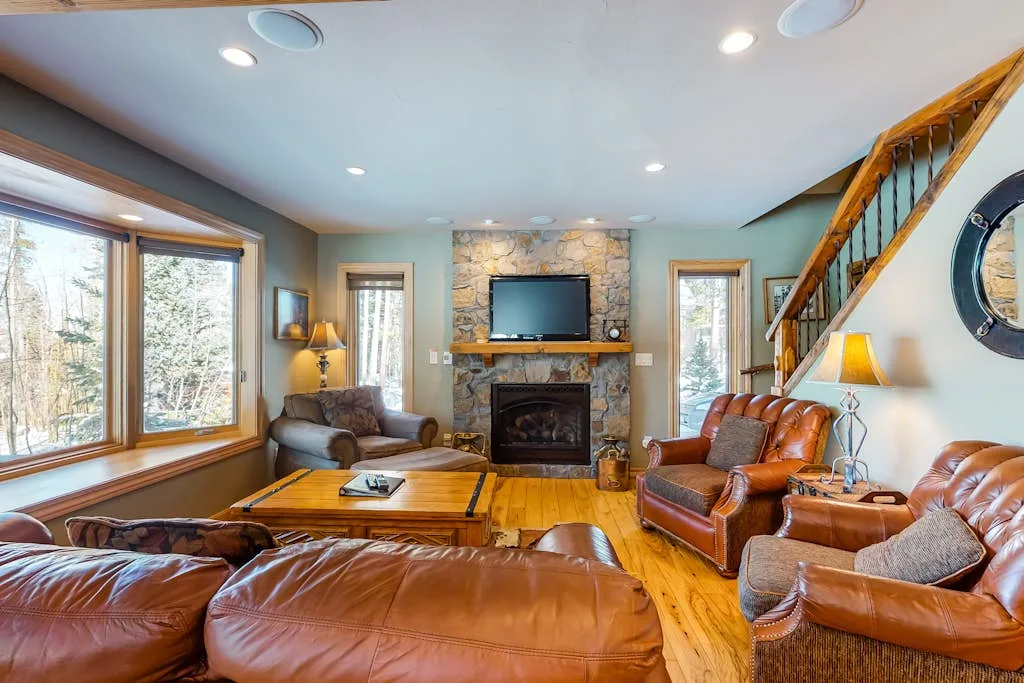 A living room with leather seating, a fireplace, and a wooden staircase.