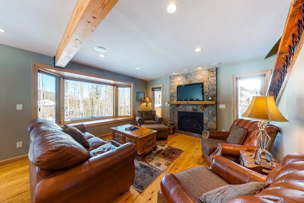A living room with leather seating, large windows, and a stone fireplace.