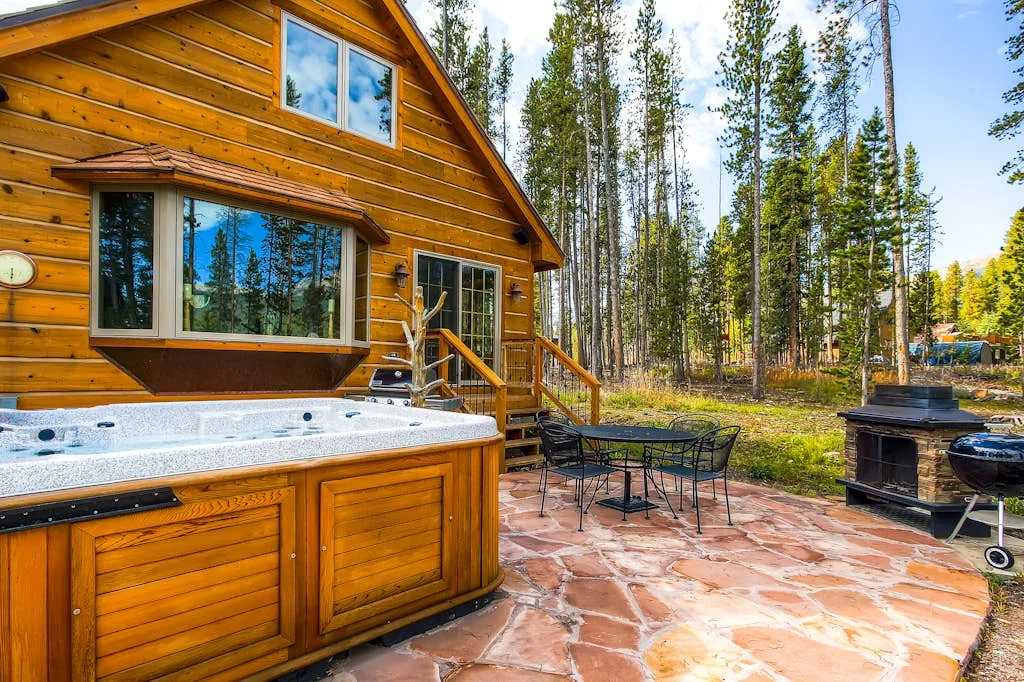 A wooden cabin patio with a hot tub, outdoor seating, and a fire pit.