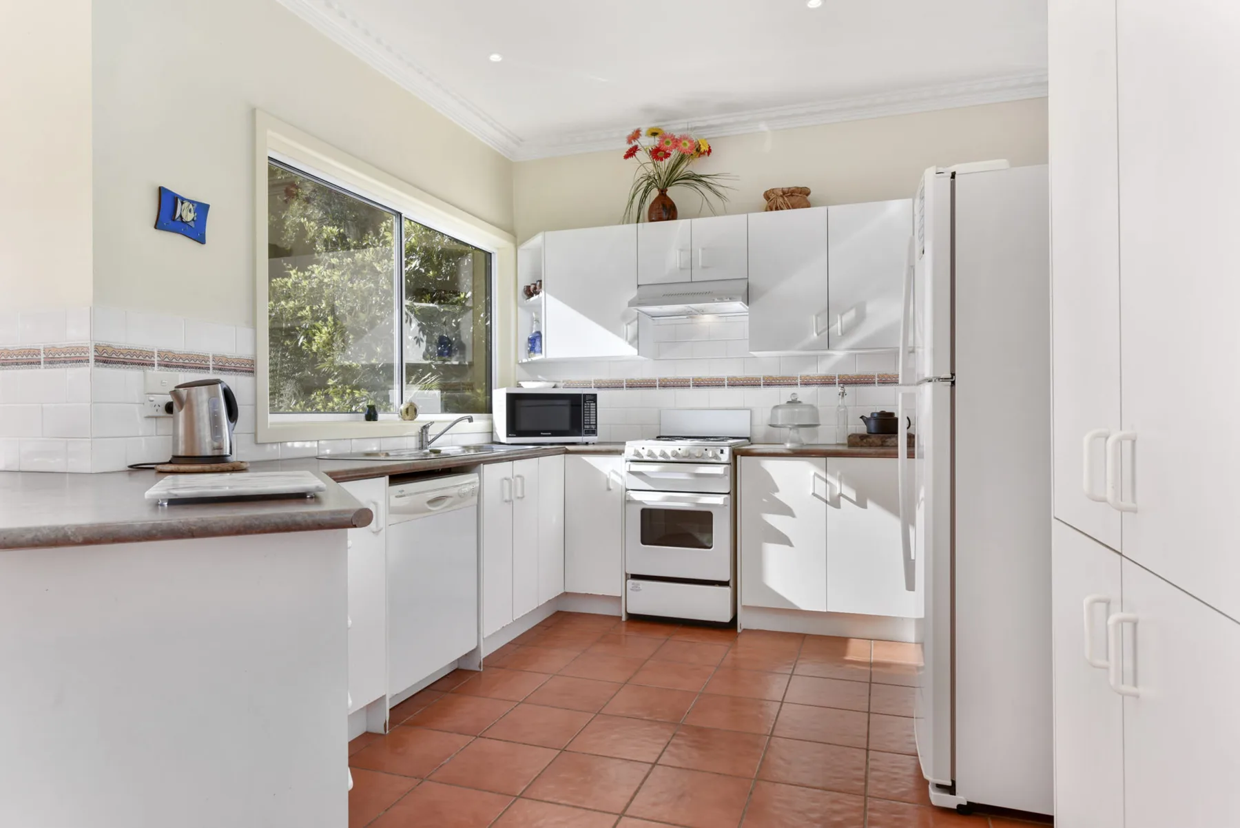 A bright kitchen with white cabinetry and a window overlooking greenery.