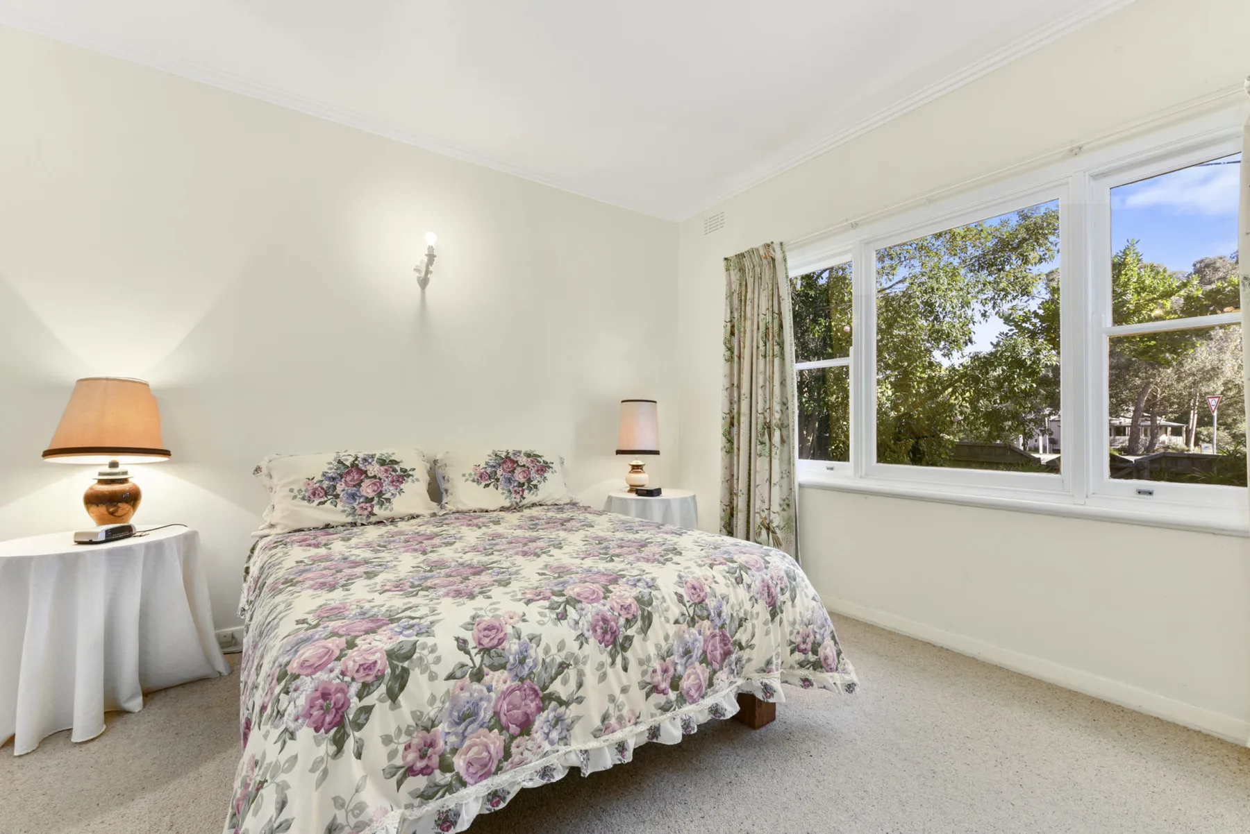 A bedroom with floral bedding and windows overlooking leafy trees.