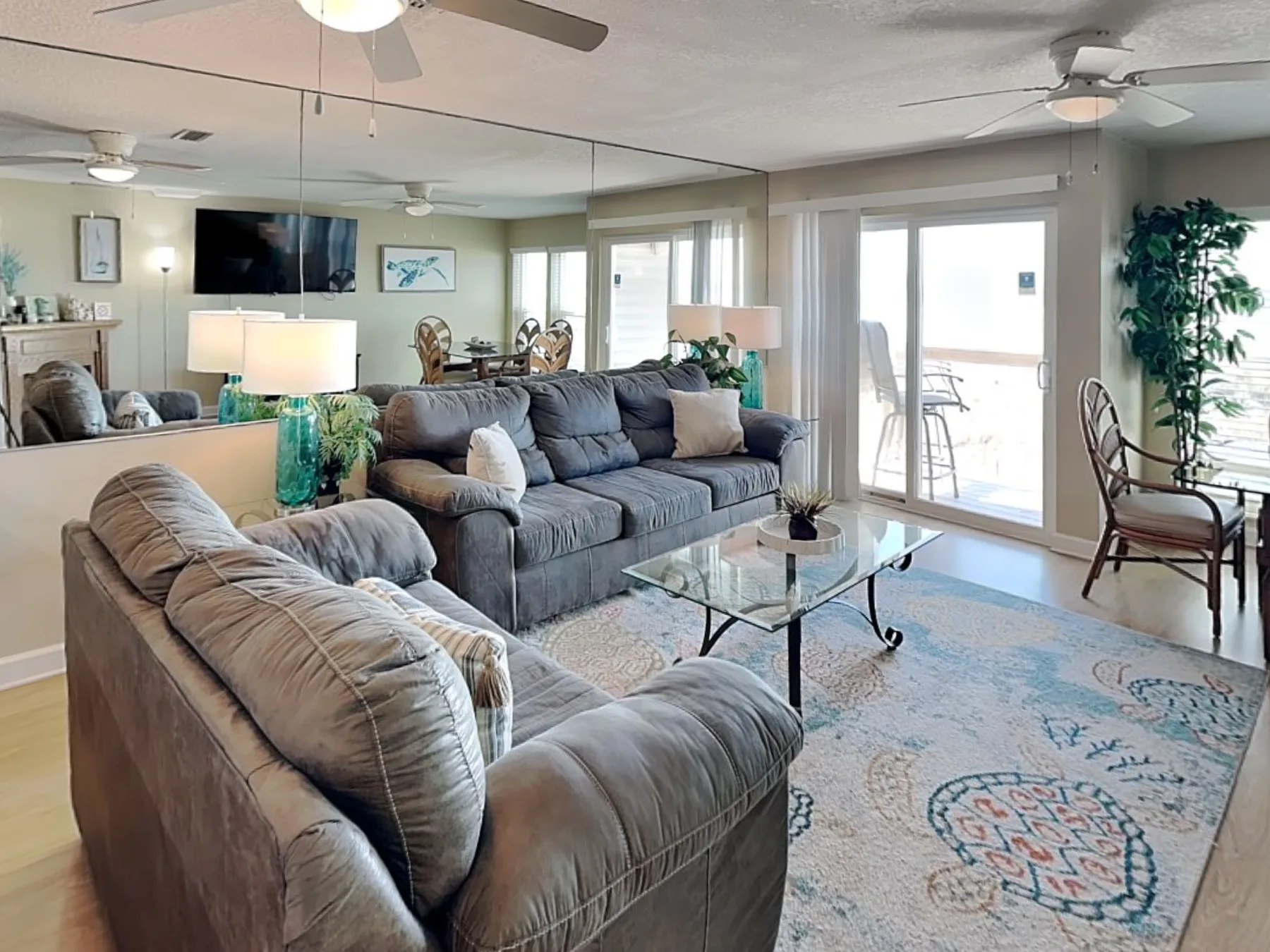 A bright living room with gray seating, a glass coffee table, and sliding doors.