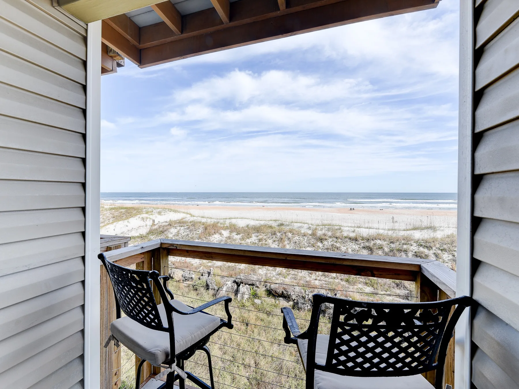 A covered balcony overlooks a sandy beach and ocean, with two chairs.