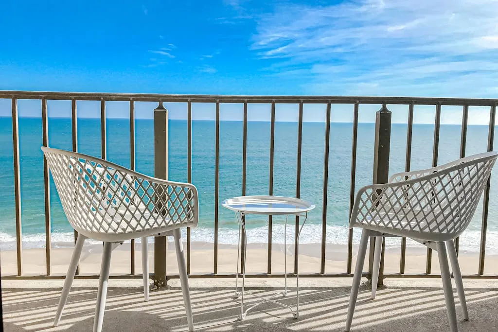 Two chairs and a small table sit on a balcony facing the ocean.