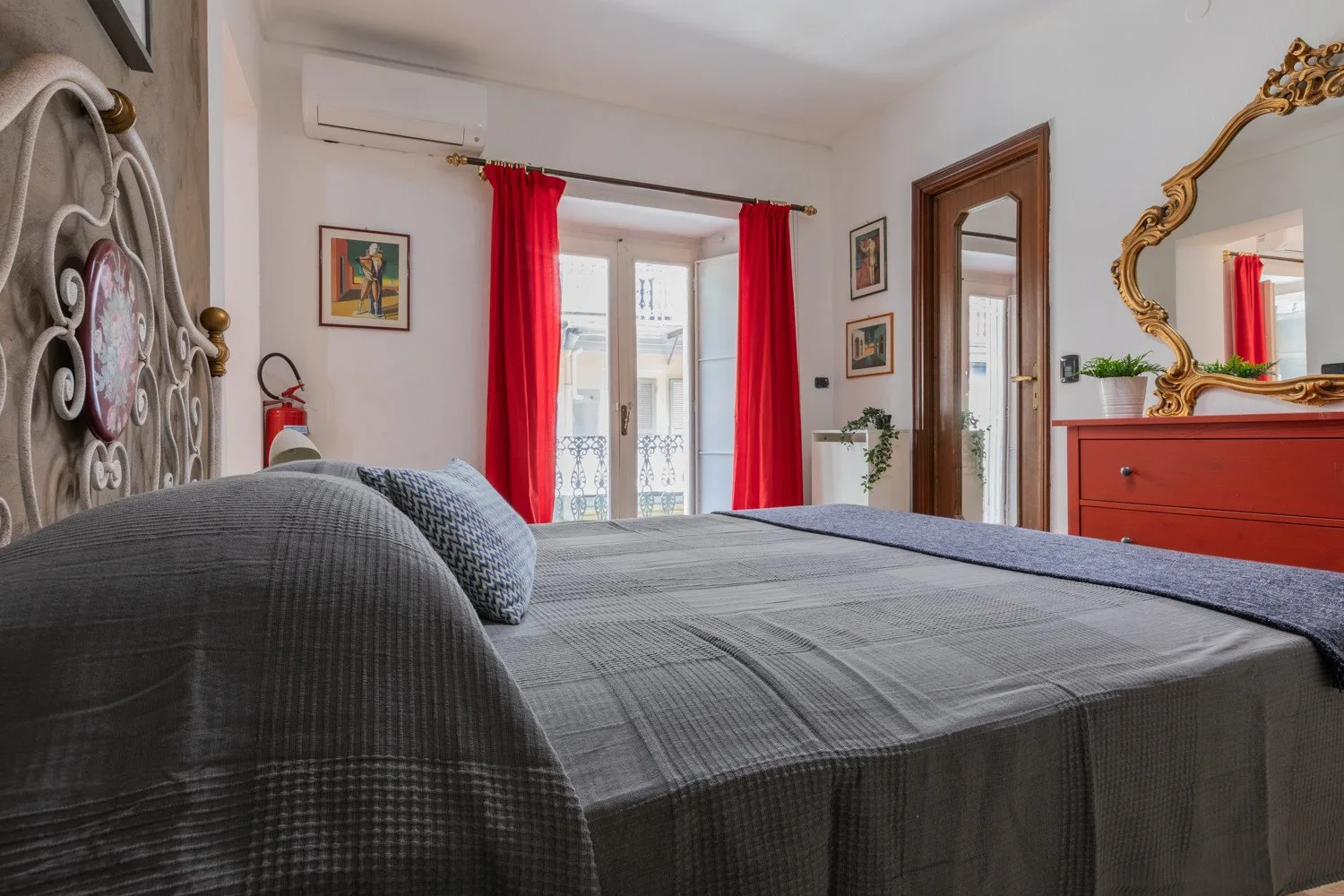 Un dormitorio con una cama tendida, cortinas rojas y un espejo de pared.