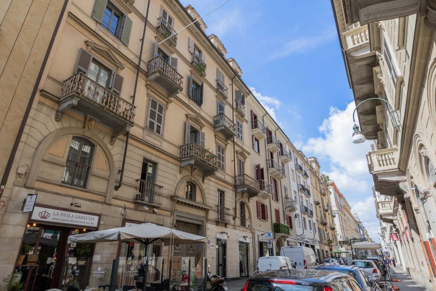 Una calle urbana con edificios de varias plantas, balcones y coches estacionados.