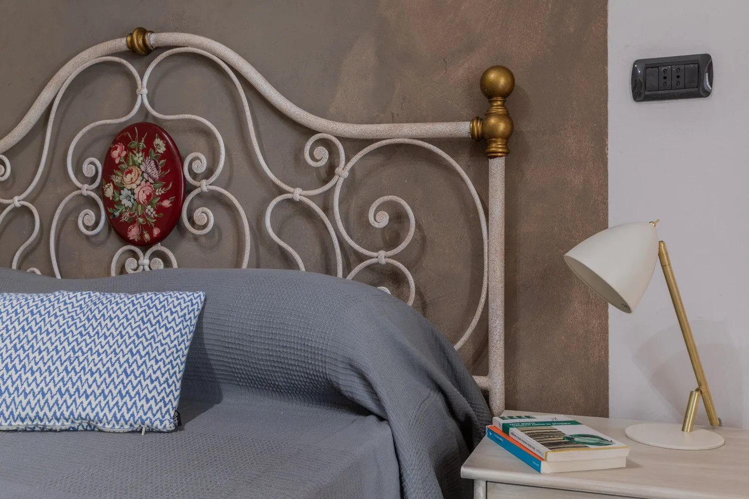 Un dormitorio con una cama gris, cojines estampados y un cabecero de metal ornamentado.