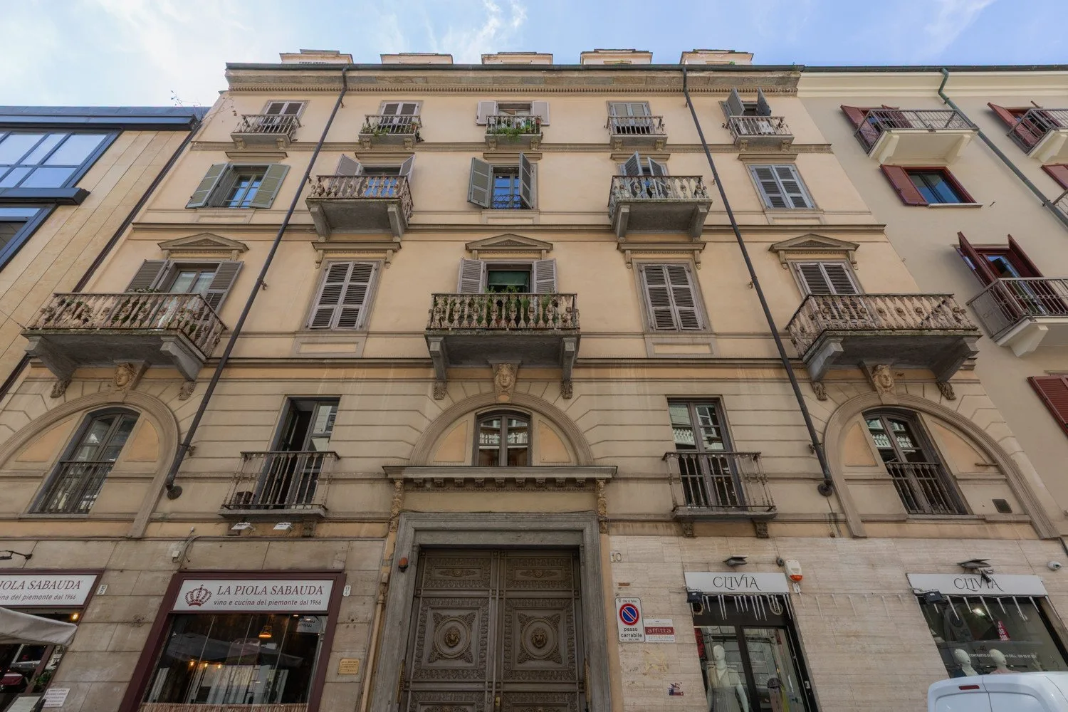 Fachada beige de un edificio de varias plantas con balcones y locales a pie de calle.
