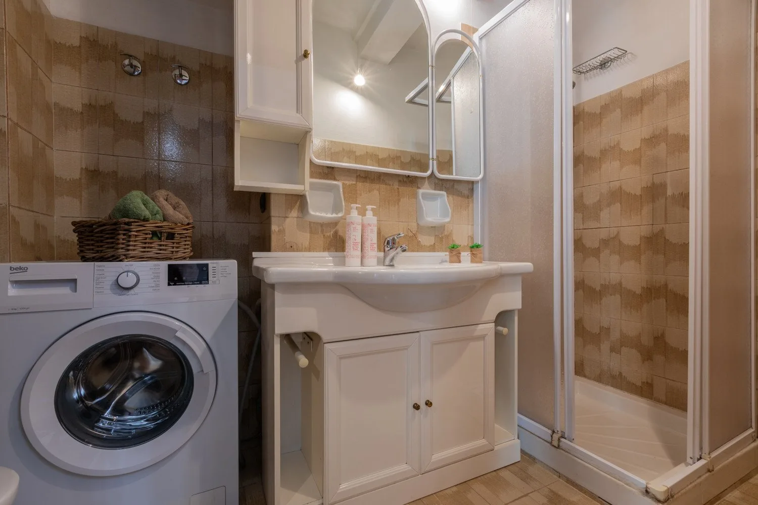Un baño con lavabo, espejo, lavadora y ducha de vidrio.