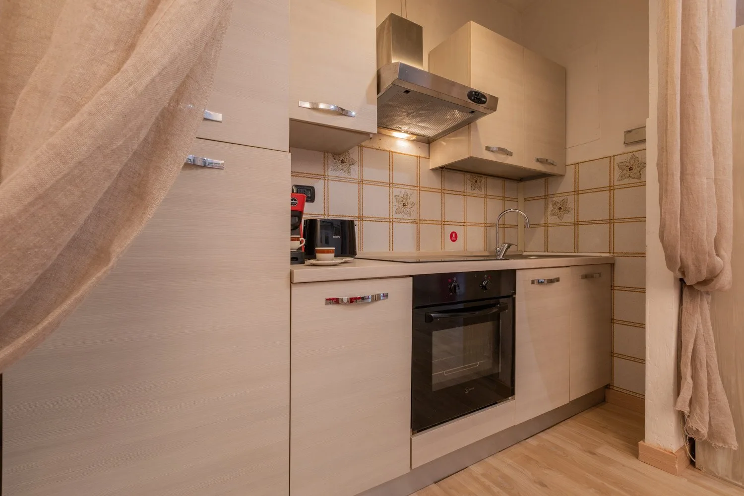 Una cocina con gabinetes claros, horno empotrado y salpicadero de azulejos.