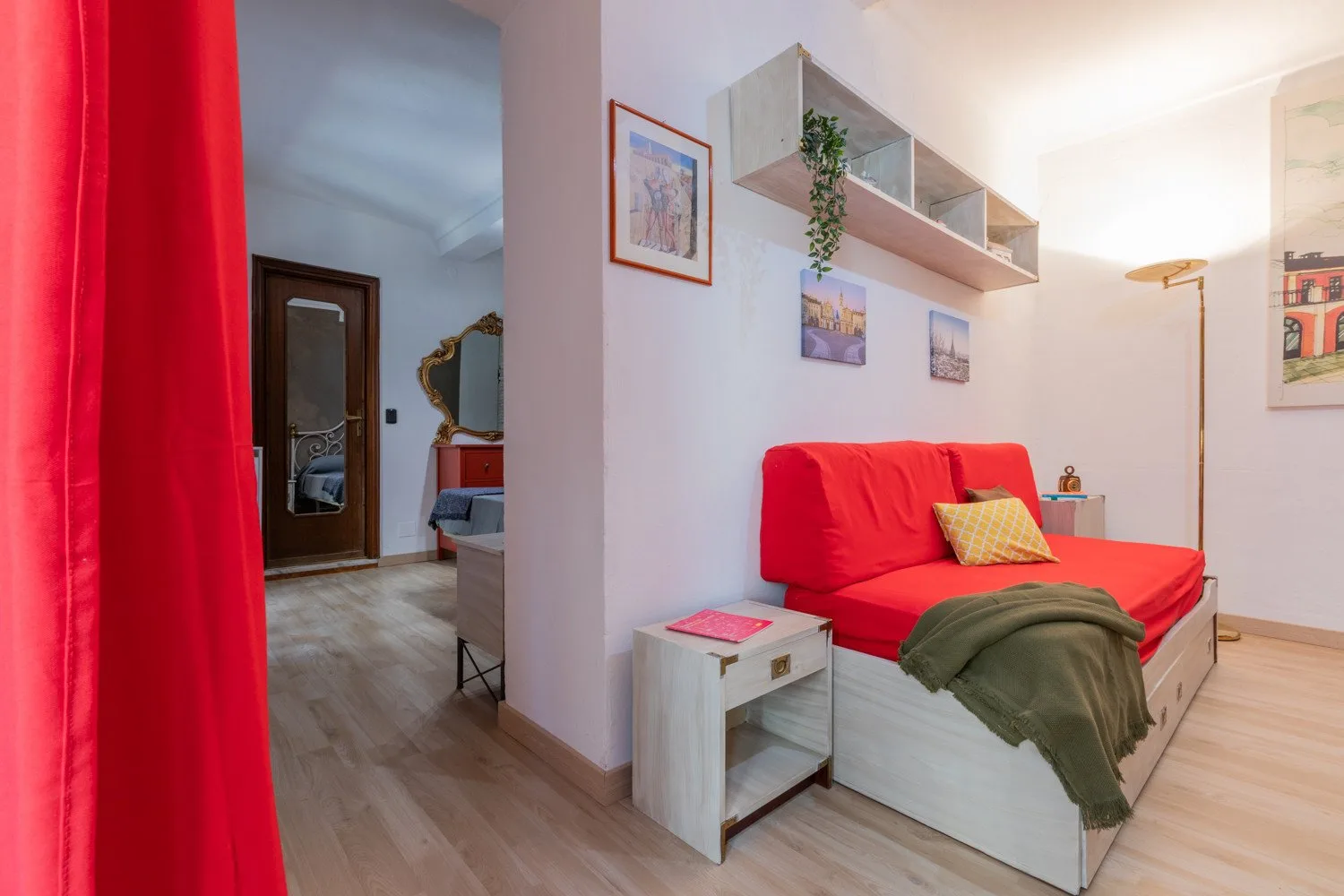 Una zona de estar con un sofá rojo, estantes de pared y una mesita auxiliar.