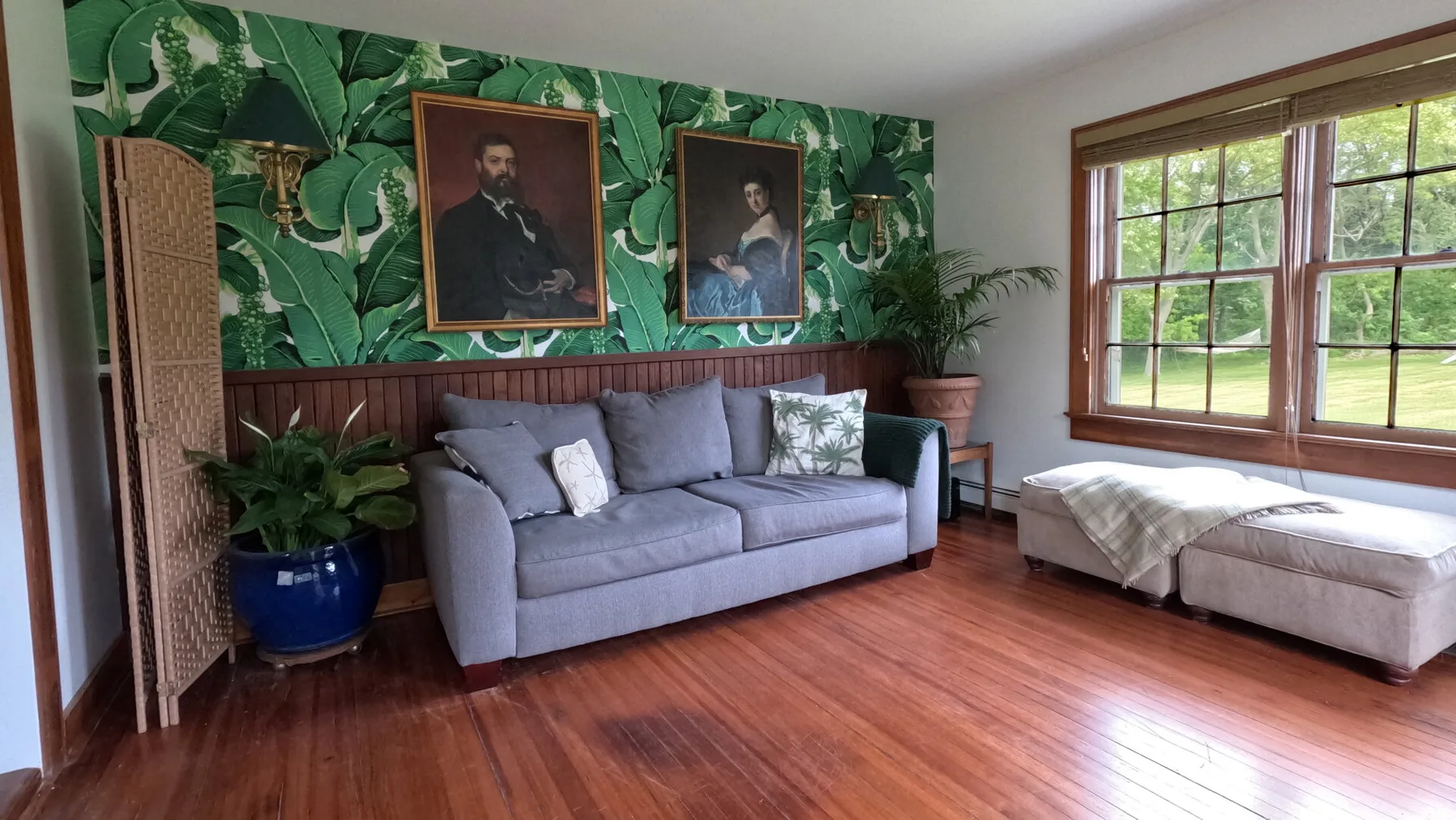 Una sala de estar con un sofá gris junto a grandes ventanas.