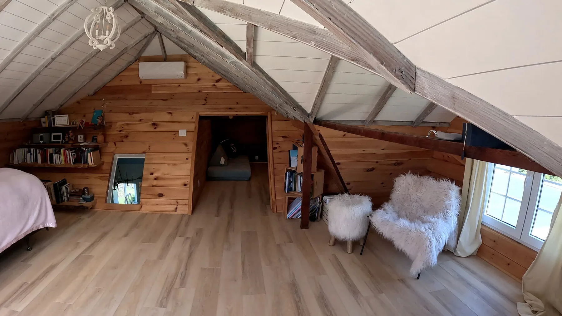 Un dormitorio abuhardillado con paredes de madera, vigas expuestas y asientos junto a la ventana.