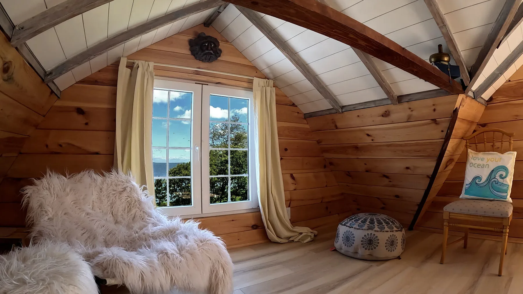 Una habitación revestida de madera con ventana, cortinas claras y un asiento bajo acolchado.
