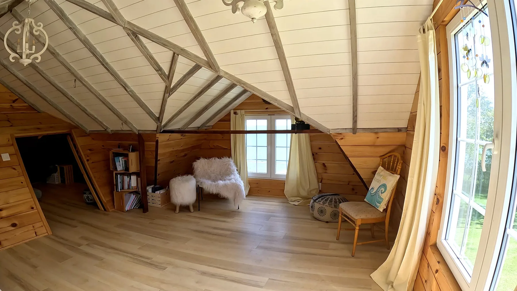 Una luminosa habitación revestida de madera, con techo inclinado, ventanas y asientos.
