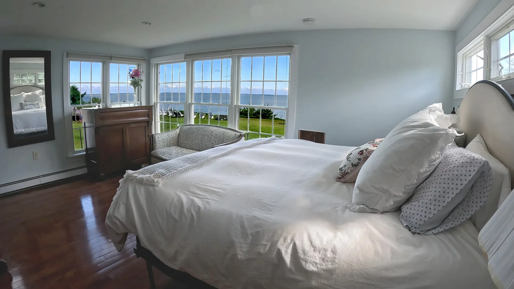 Un dormitorio luminoso con una cama junto a grandes ventanas con vista al agua.