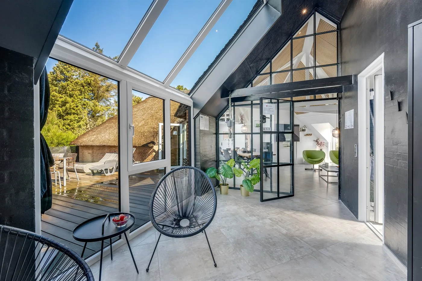 Una sala luminosa con techo de vidrio se abre a una terraza de madera.