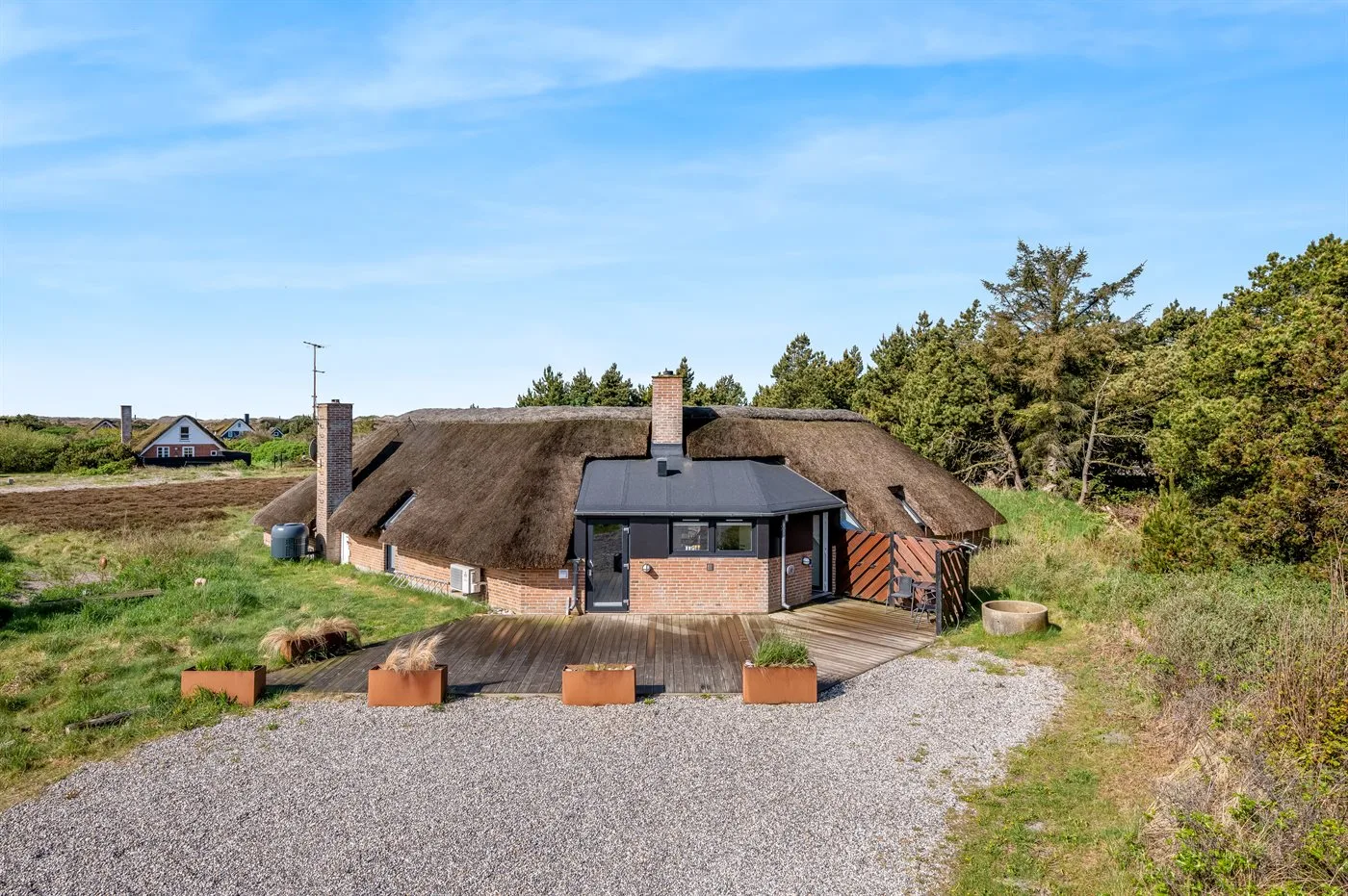 Una casa con techo de paja se encuentra junto a un camino de grava y campos verdes.