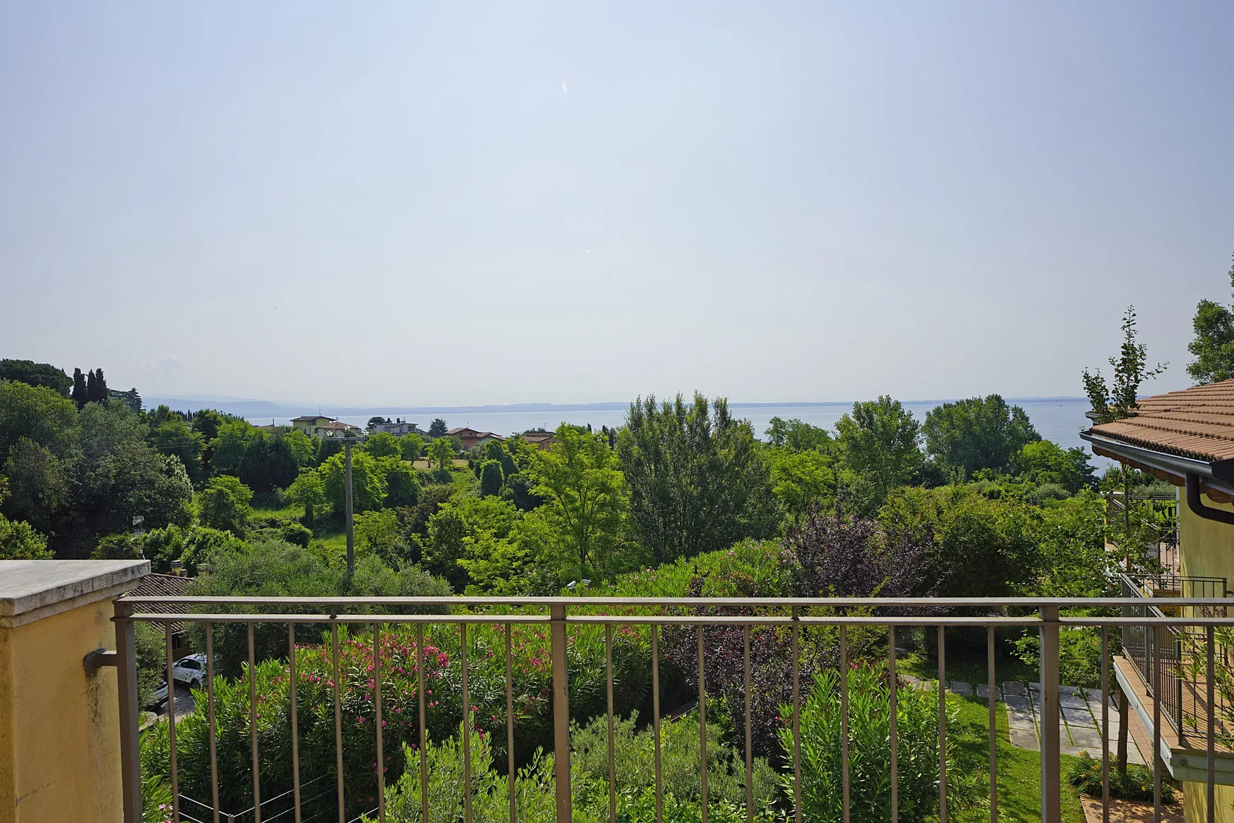 Un balcón da a jardines frondosos y una vista costera a lo lejos.